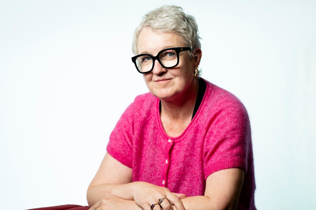 Imogen Tyler, smiling, in black-framed glasses and a pink cardigan, against a white background